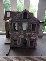 Front view of the antique wooden doll house showing peeling paint on facade with window and door openings.