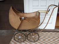 Side view showing the woven wicker body, scalloped design edge, metal wheels and handle with rust and wear.