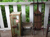 Green metal trunk, wooden sled with rust, and small wooden table on porch.