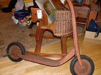 Wooden rocking horse with carved dog-shaped head and wicker basket attached to the back of the seat