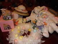 Photo showing assortment of Easter hats, feather wreath with colored eggs, stuffed Easter Rabbit dolls, and hollow bunny tail light on table.