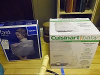Photo of both boxed items: Inglesina Fast table chair and Cuisinart Baby steam sterilizer on a wooden floor with books in background