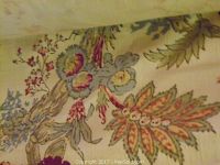 Close-up of fabric showing floral and botanical design with pastel colors including blue, yellow, and muted red