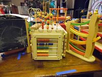 Wooden multi-activity cube showing bead maze top with colorful wires and beads, and small wooden framed chalkboard in background