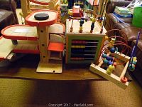 Photo showing wooden airplane landing pad, wooden abacus, and bead maze toys on a table.