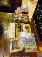 Overview of assorted children's toys and games including wooden school bus bead maze, boxed board book sets, toy iron, and board games stacked on a table.