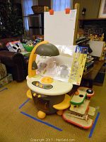 Small yellow and gray children's kitchen play set with stove, sink, and utensil features, shown next to a large upright board.