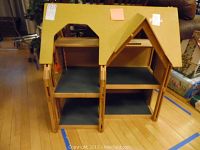 Front view of a large wooden dollhouse with multiple open floors, showing two roof peaks and blue floors inside.