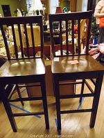 Two wooden stools shown side by side from the front revealing dark wood finish and vertical slatted backs, seat surfaces show scratches.