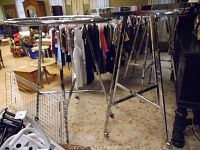 Photo showing multiple metal display racks from side angle with hanging clothes and other items around