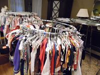 Two round metal display racks shown among clothing racks and furniture interior, displaying garments on hangers around them