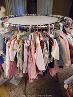 Round metal clothing display rack filled with children's clothing on hangers showing various pastel and light colors.