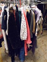View of assorted children's clothes hanging on hangers, including dresses and tops in various colors and textures such as faux fur and floral prints.