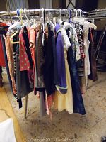 Photo displaying a rack of assorted children's clothing including dresses, tops, and pants in various colors and sizes.