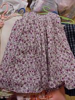 White dress with pink and purple flower pattern on pink hanger with other clothing visible