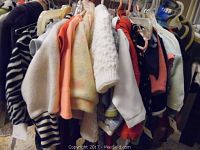 Various children's clothes hanging on a rack including sweaters, dresses and tops in assorted styles and colors