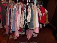 Photo showing a rack with approximately 30-40 assorted pieces of boy and girl clothing in various colors and styles hung on hangers.