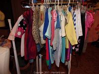 Photo showing clothing items on hangers including dresses, shirts, and tops in various colors and sizes.