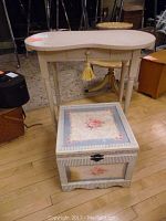 Vintage cream kidney-shaped vanity table with center drawer and tassel pull, photographed standing on floor with metal and wooden items in background, showing full front and side view