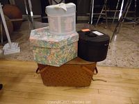 Full view of four containers including one large brown woven picnic basket, a floral octagonal box, a round vintage-label covered box, and a black oval box.