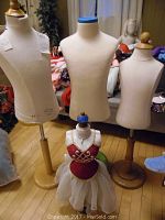 Four mannequins shown together; three fabric torso mannequins on wooden stands and one smaller decorative mannequin dressed in a red and white outfit.