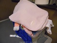 Blue plastic tote filled with assorted boys and girls clothing, covered by a large pink fabric item.