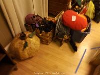 Large and medium-sized metal Halloween pumpkins with spiral cut-out designs, plush pumpkin pillow, and miscellaneous holiday decorations in basket and bin.