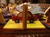 Wooden bookends shaped like a red car with a beige deer figure attached on a yellow base