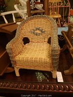 Photo of a wicker doll chair with woven seat and back, featuring a grey and beige pattern and rounded backrest