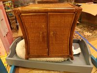 Closed woven doll cabinet showing wicker texture and wooden frame with handles