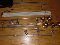 Full view of multiple metal and white plastic track lighting sections, adjustable metal track heads, and five brass dome ceiling lamps arranged on wood floor.