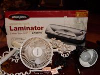 Photo of Wilson Jones laminator box, small white desk fan with plastic blades and cord, and parts of ceiling lamp fixtures on table.