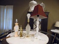 Four table lamps placed on a round white table inside a room, showing details of bases and one lampshade.