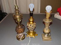 Four brass and ceramic table lamps displayed side by side, showing varied shapes, finishes, and sizes between 13-15 inches tall.