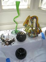 Full lot display showing green twisted vase, copper train sculpture, colorful abstract glass sculpture, and two black glass bowls on white cloth