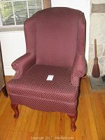 Front angle view of maroon wing chair showing upholstery and wooden legs