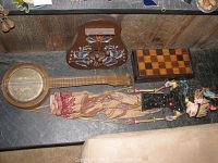 Full lot view showing vintage banjo, wooden checkerboard, and Indonesian hand carved puppet arranged on surface