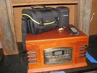 Crosley Music Center in wooden cabinet showing front control panel with display, placed on a shelf with accessories on top.
