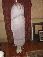 Full view of white chiffon 1920s costume on dress form against curtain background showing full length dress and matching lace-up boots.