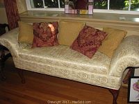 Full view of the cream brocade upholstered settee and five decorative pillows.