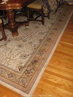 Close view of the beige Hamadan traditional patterned wool rug beneath dining table showing floral and geometric design, some soiling