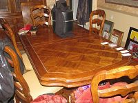 Front angled view showing the table with a geometric inlaid wood pattern on the top, surrounded by wooden dining chairs with beige upholstered seats.