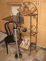 Full view of 3-tier black metal wire rack, black metal chair, stainless steel ice bucket on stand, two woven baskets with fabric linings on lower shelves