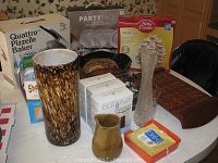Overview of lot showing cupcake stand, Quattro pizzelle baker box, glass vases, wood tray, and other items on table
