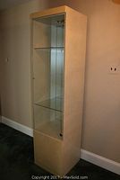 Full view of the tall beige laminate display cabinet showing the solid bottom and glass top doors with mirrored back and glass shelves inside.