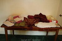 Overview of assorted folded table linens, napkins, pillowcases on a wooden table