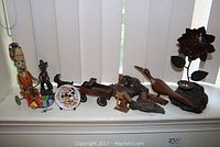 Wide view showing entire lot on windowsill including tin toys, wooden birds, metal goat and wagon, figurines, and sunflower candle holder.