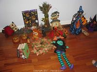 Full assortment of Halloween and autumn decorations on wooden floor including witch doll, owls, pumpkins, scarecrow, and leaves garland.