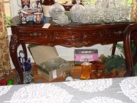 Full view of wood side table with various glassware on top, showing the detailed carved front and three drawers