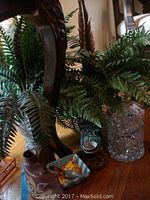 Photo showing two faux fern plants, cut glass vase, and a small three-piece ceramic set including a teapot, cup, and bird motif ashtray beneath wooden furniture.